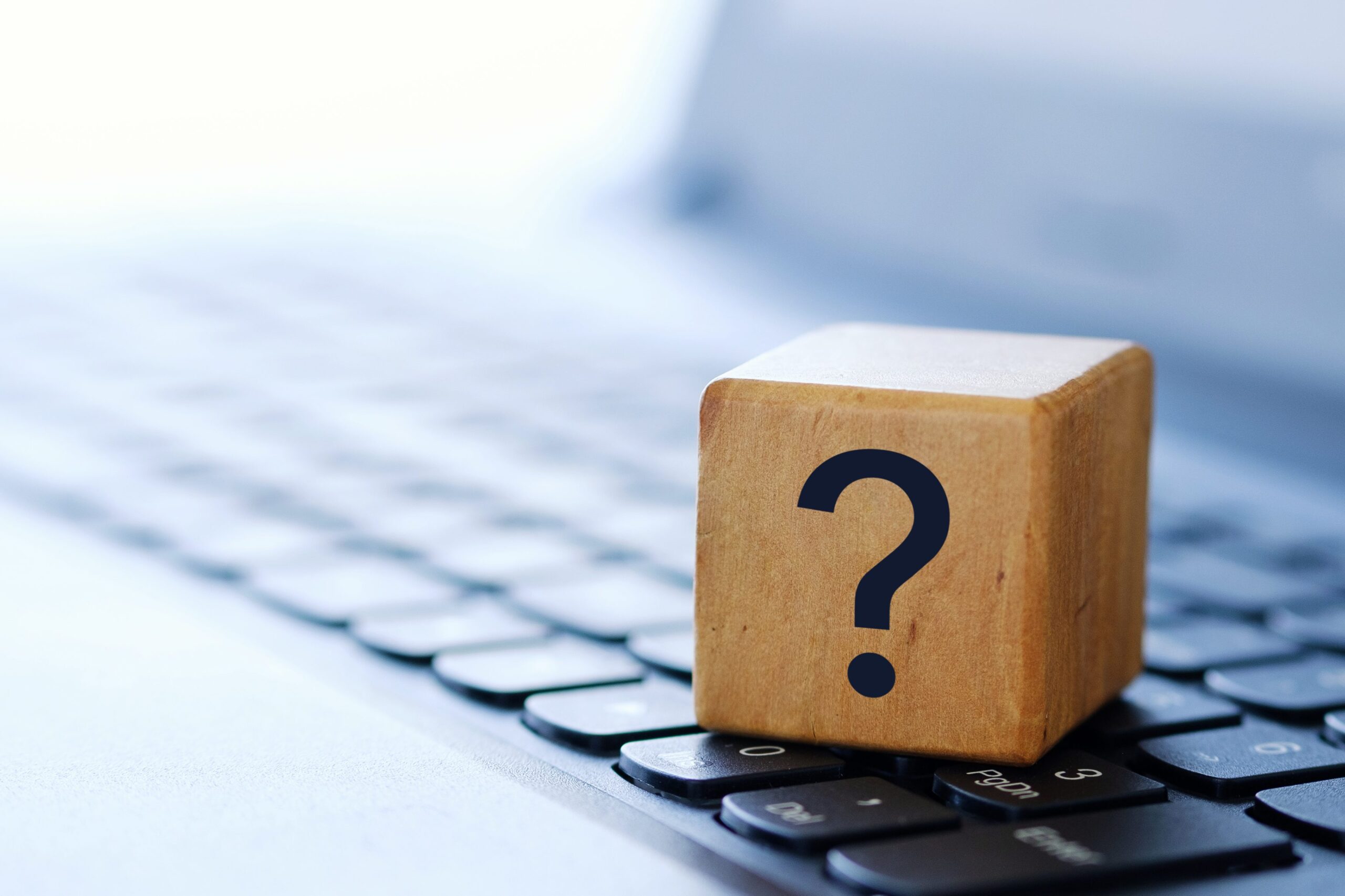 A question mark on a wooden cube, on a computer keyboard
